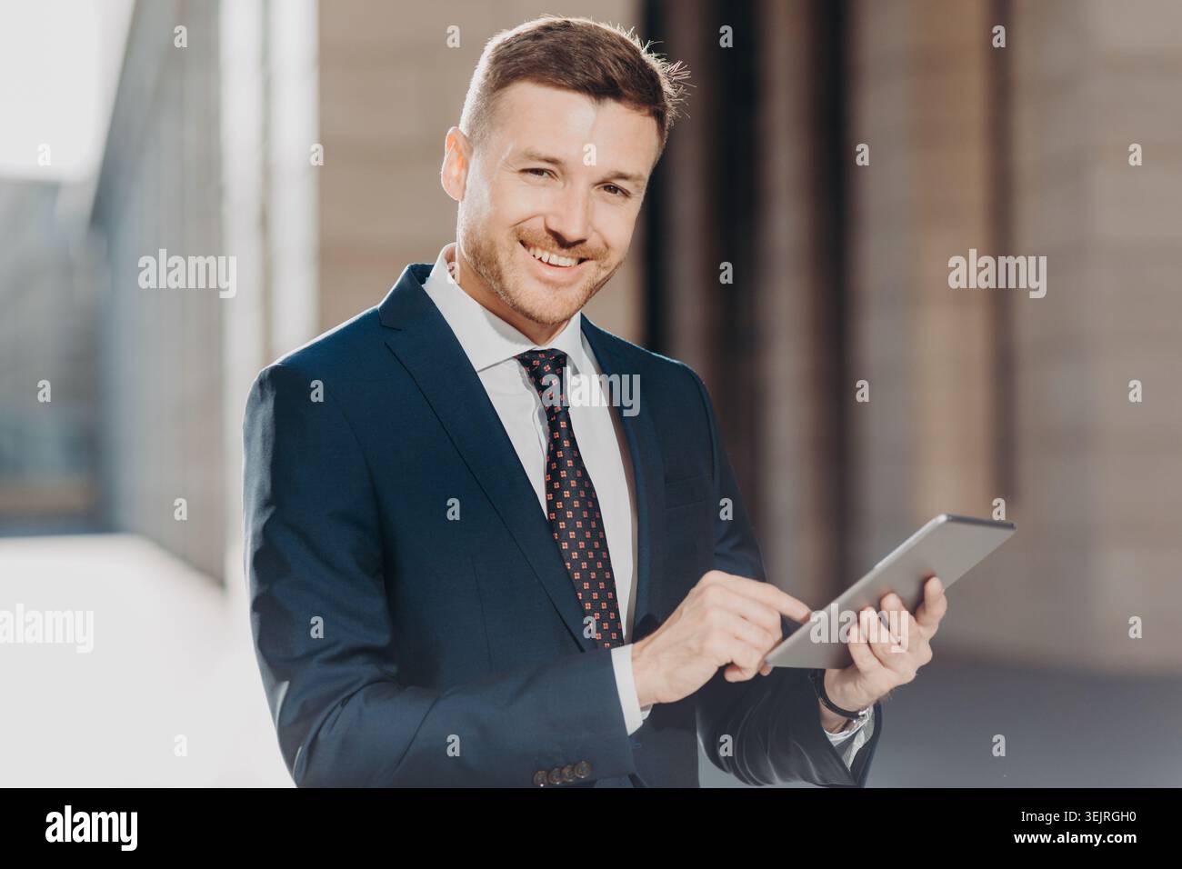 Smiling businessman uses digital tablet outside modern office building Stock Photo