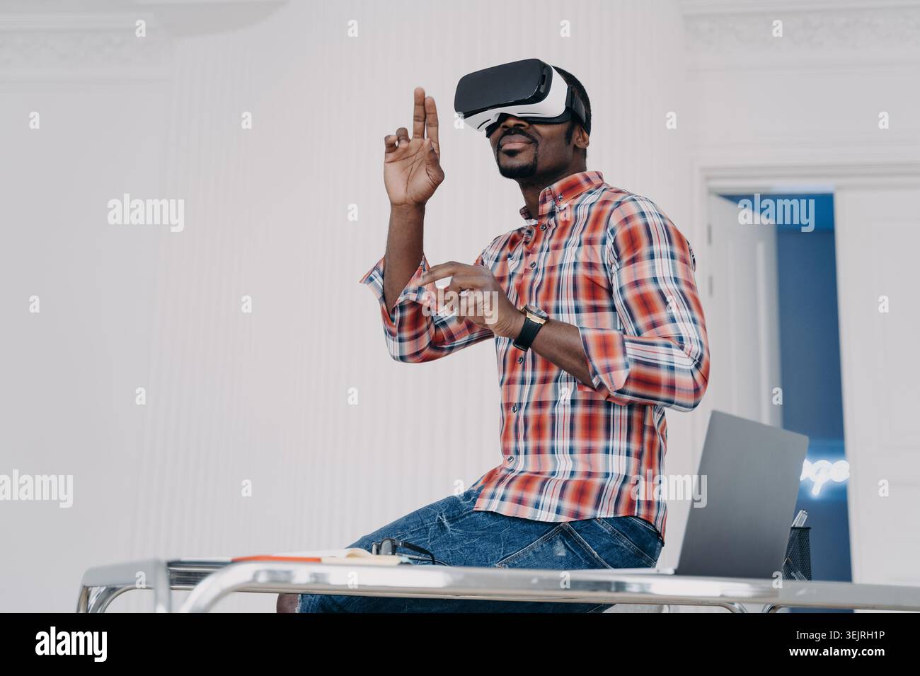 Young man using virtual reality headset while gesturing at desk in office Stock Photo