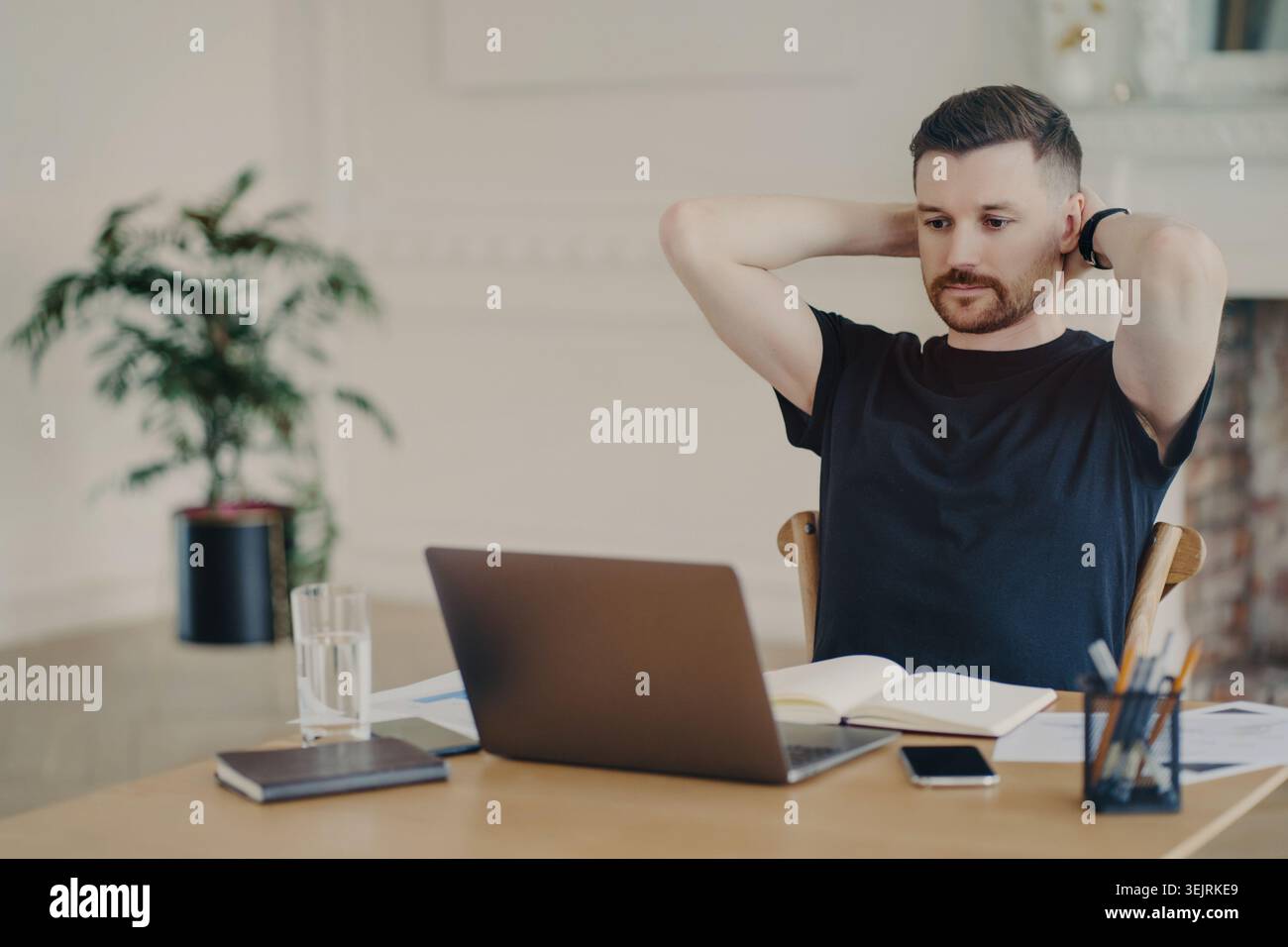 Caucasian man stretches with hands behind head while working on laptop in home office Stock Photo