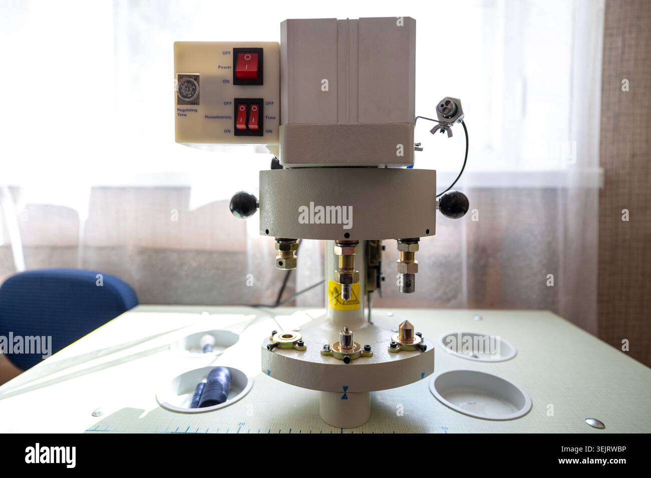 An industrial automatic button and rivet setting machine with red rocker switches on the electrical control panel is positioned on a worktable surface Stock Photo
