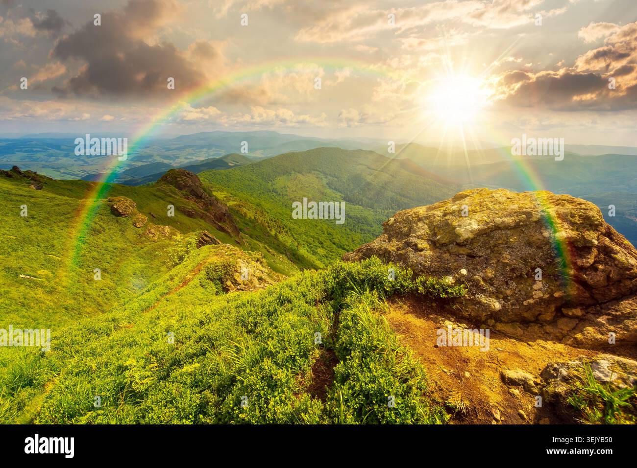 sunset over picturesque mountainous countryside scenery. dynamic sky above the distant valley. green meadows and rocks on the hill. wonderful nature s Stock Photo