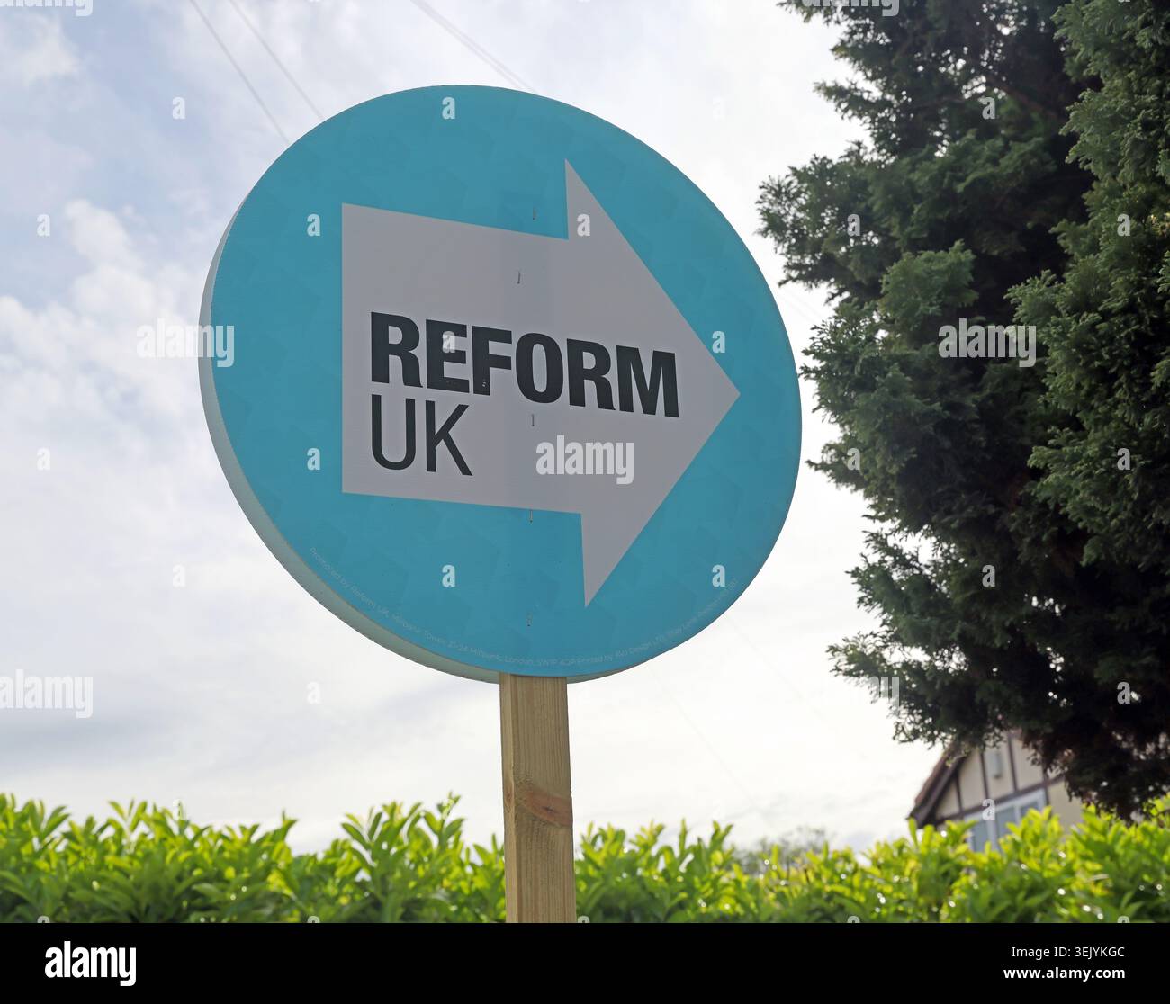 Blue ReformUK arrow sign rises above a garden hedge as Makerfield voters prepare for the June 2026 by-election. Stock Photo