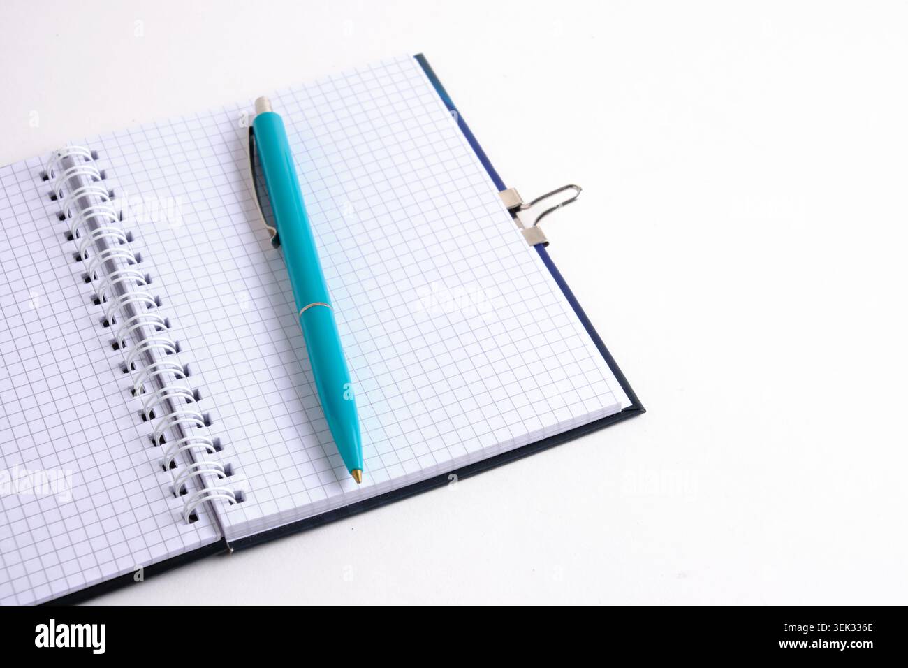 Turquoise pen lies diagonally on an open spiral squared notepad on white background. Angled view Stock Photo
