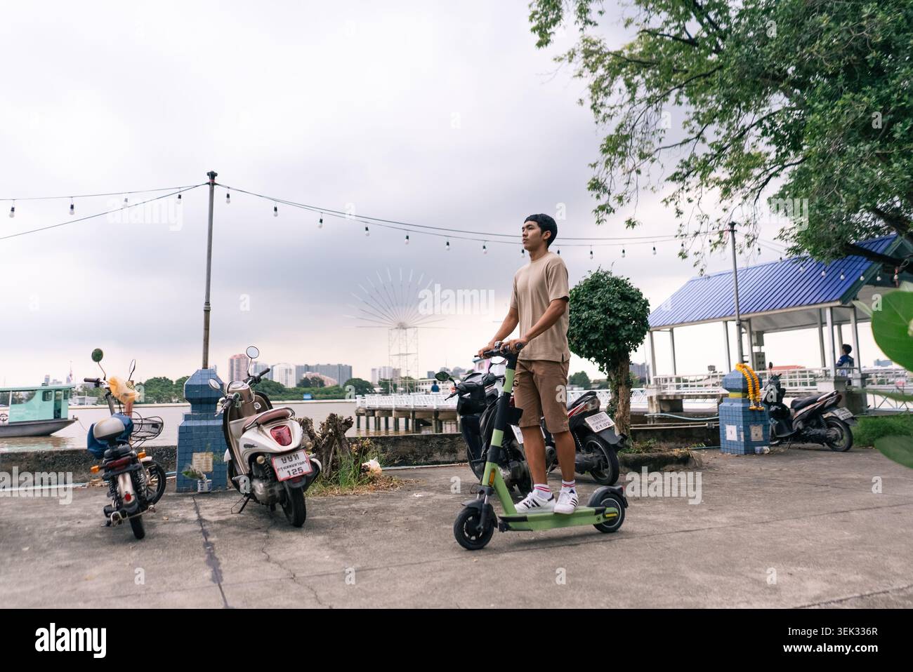 Young man riding electric scooter along tropical city waterfront Stock Photo