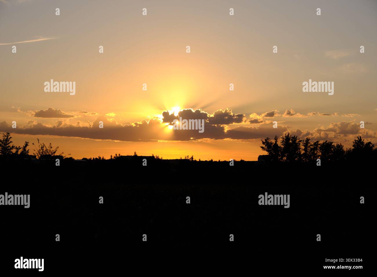 Beautiful dramatic sunset sky with golden sun rays breaking through dark clouds over silhouette Stock Photo