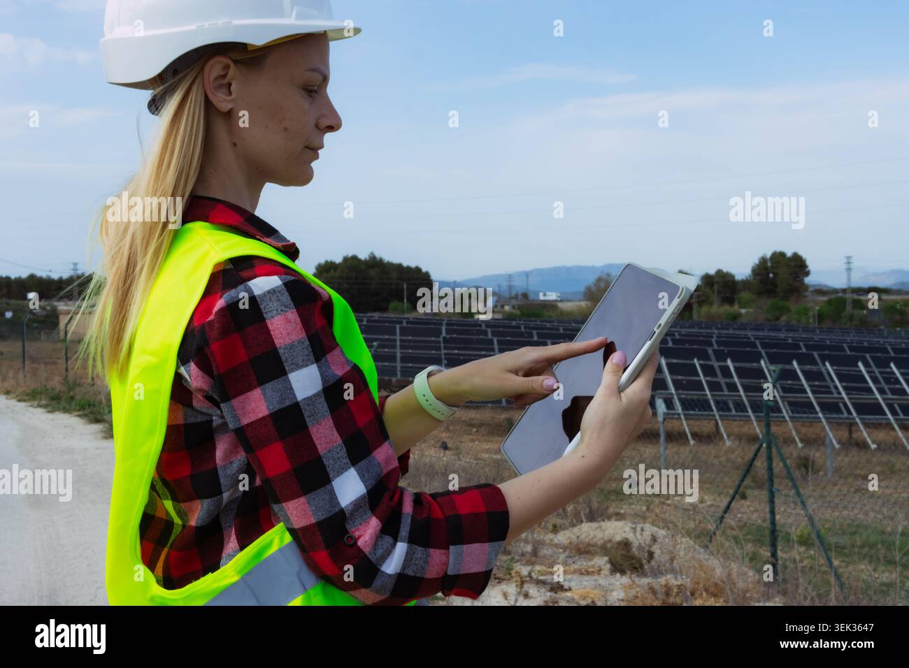 Woman engineer using a digital tablet for data analysis and management, ensuring efficient operations and maintenance of a solar power station while p Stock Photo