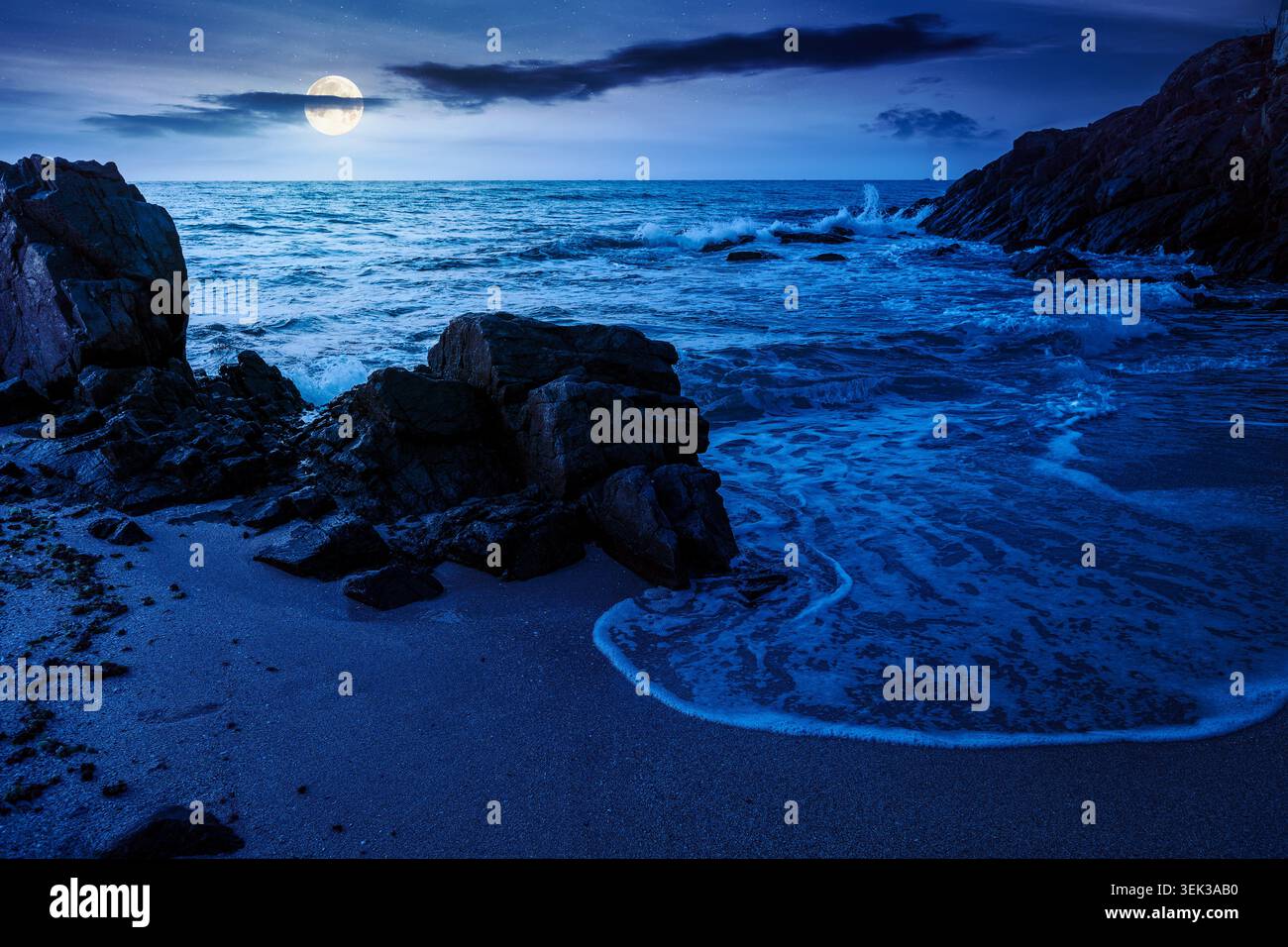 huge stones on the sandy beach at night. mysterious holiday season background at the sea. full moon over clouds on the dark sky above horizon. view of Stock Photo