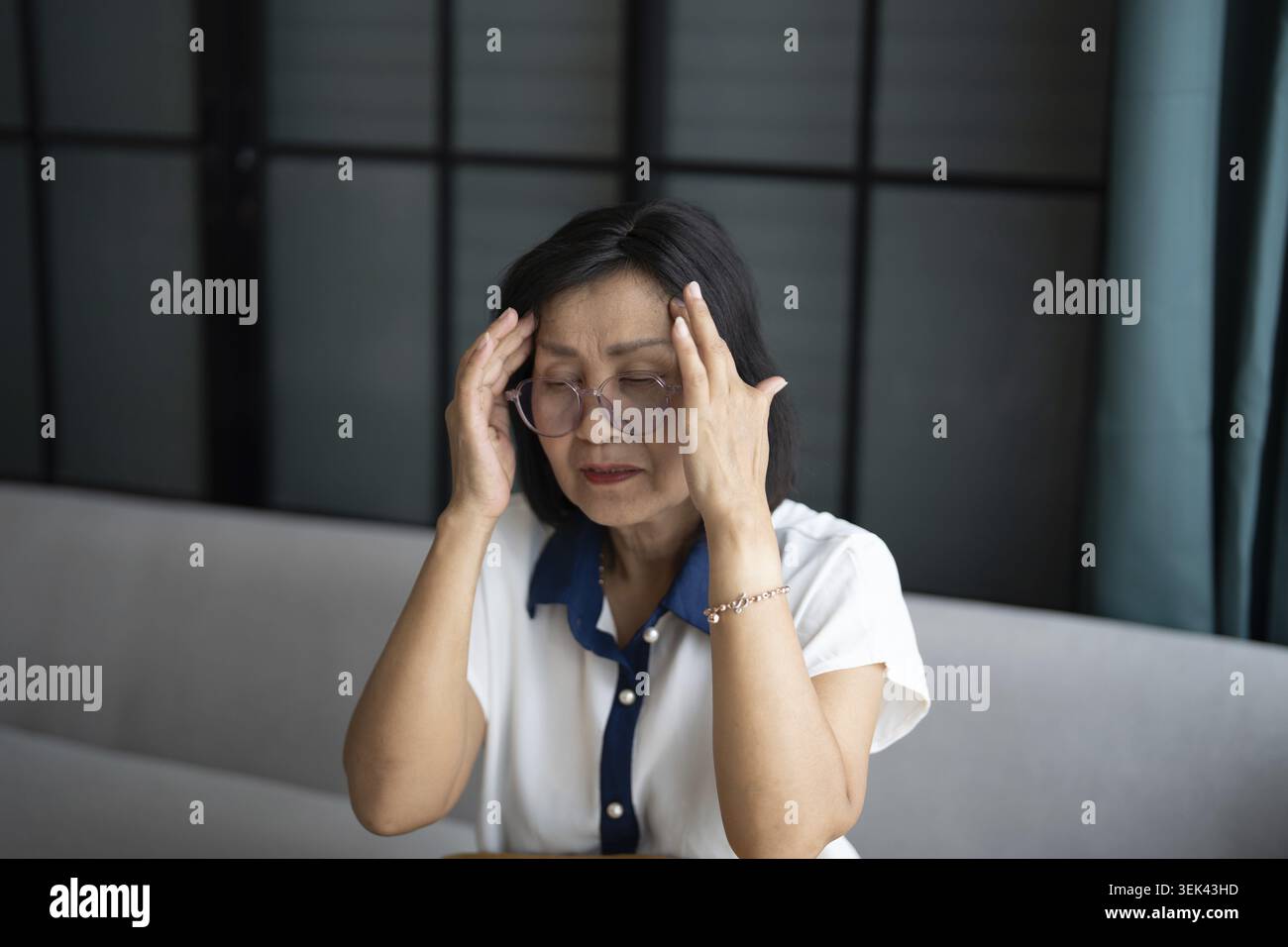 Mature Asian woman having migraine headaches at home with health concerns Stock Photo