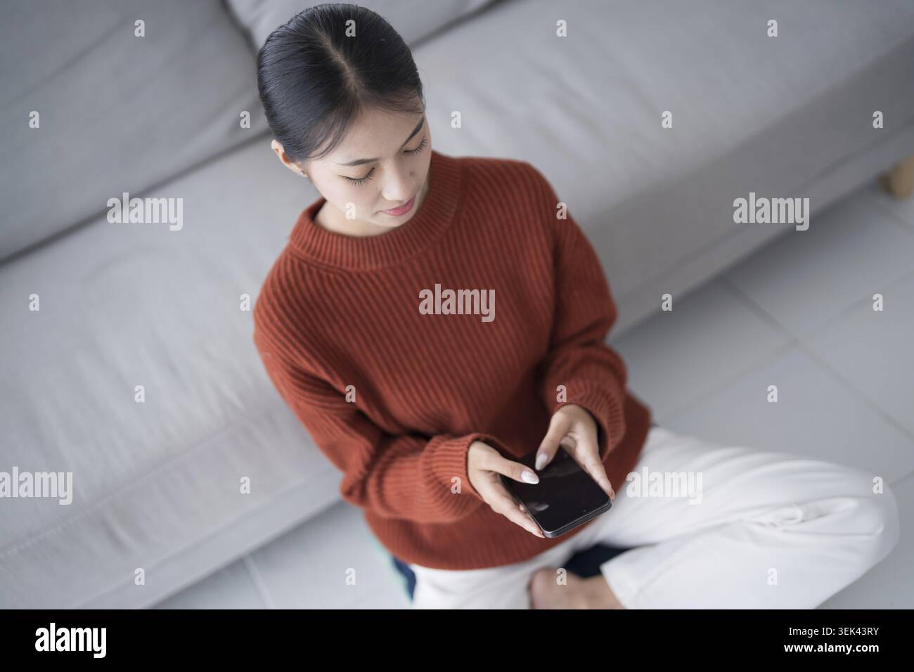 Asian woman controls smart home. Mobile phone with smart home app in the living room. Touch screen AI technology. Remote control system for your home Stock Photo