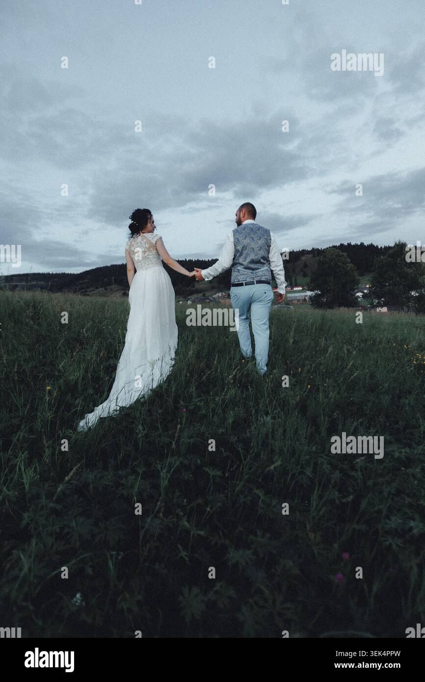 Couple walks hand-in-hand through tall grass Stock Photo