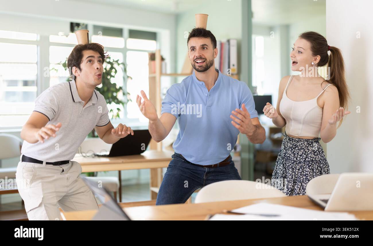 Office workers balancing cups on head enjoying their break time Stock Photo