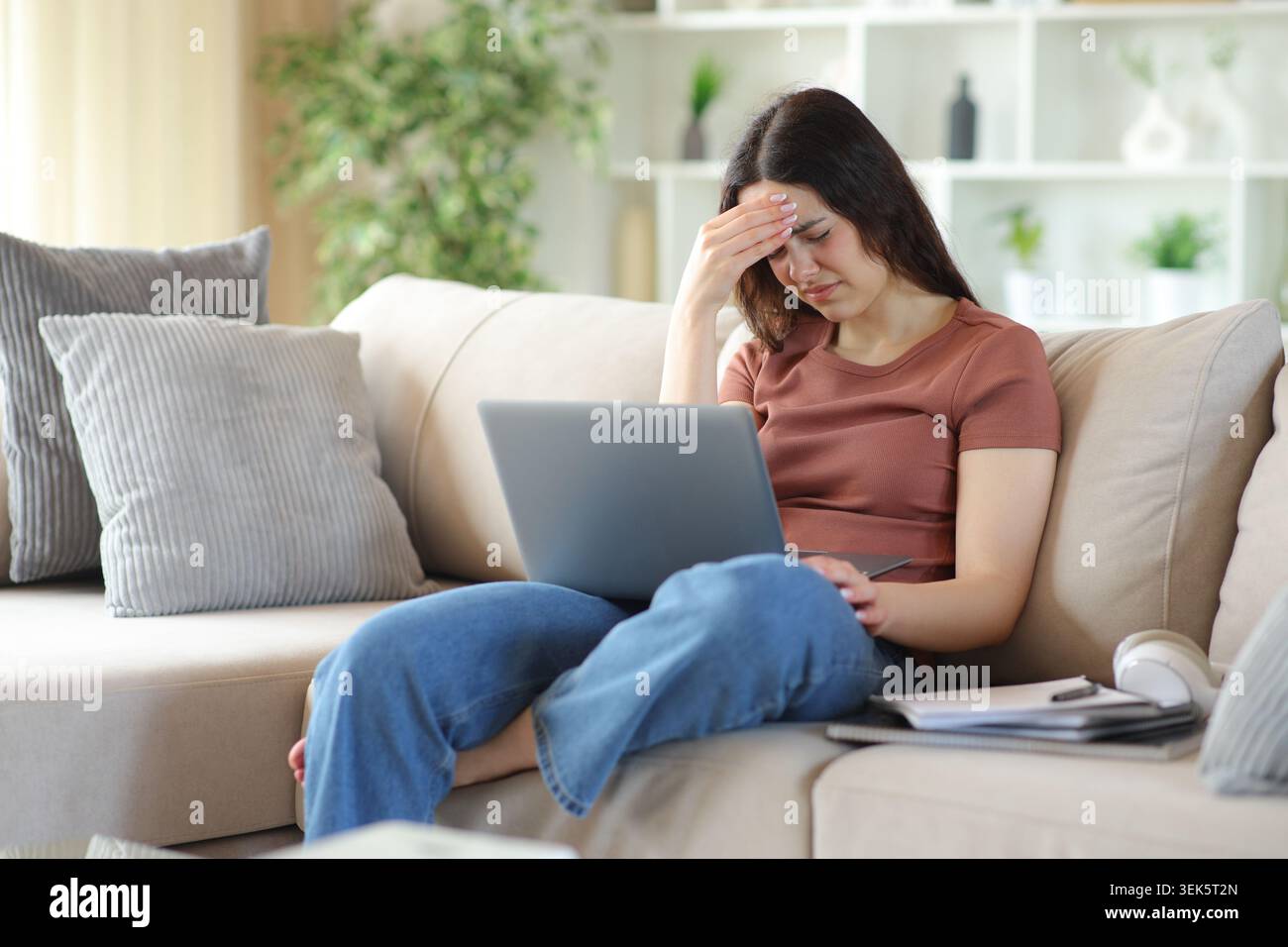 Young student suffering head ache e-learning sitting on a couch at home Stock Photo