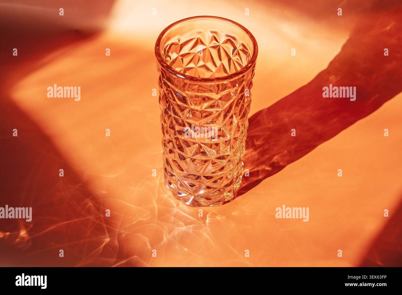 Textured glass vase casting dramatic shadows on an orange background Stock Photo