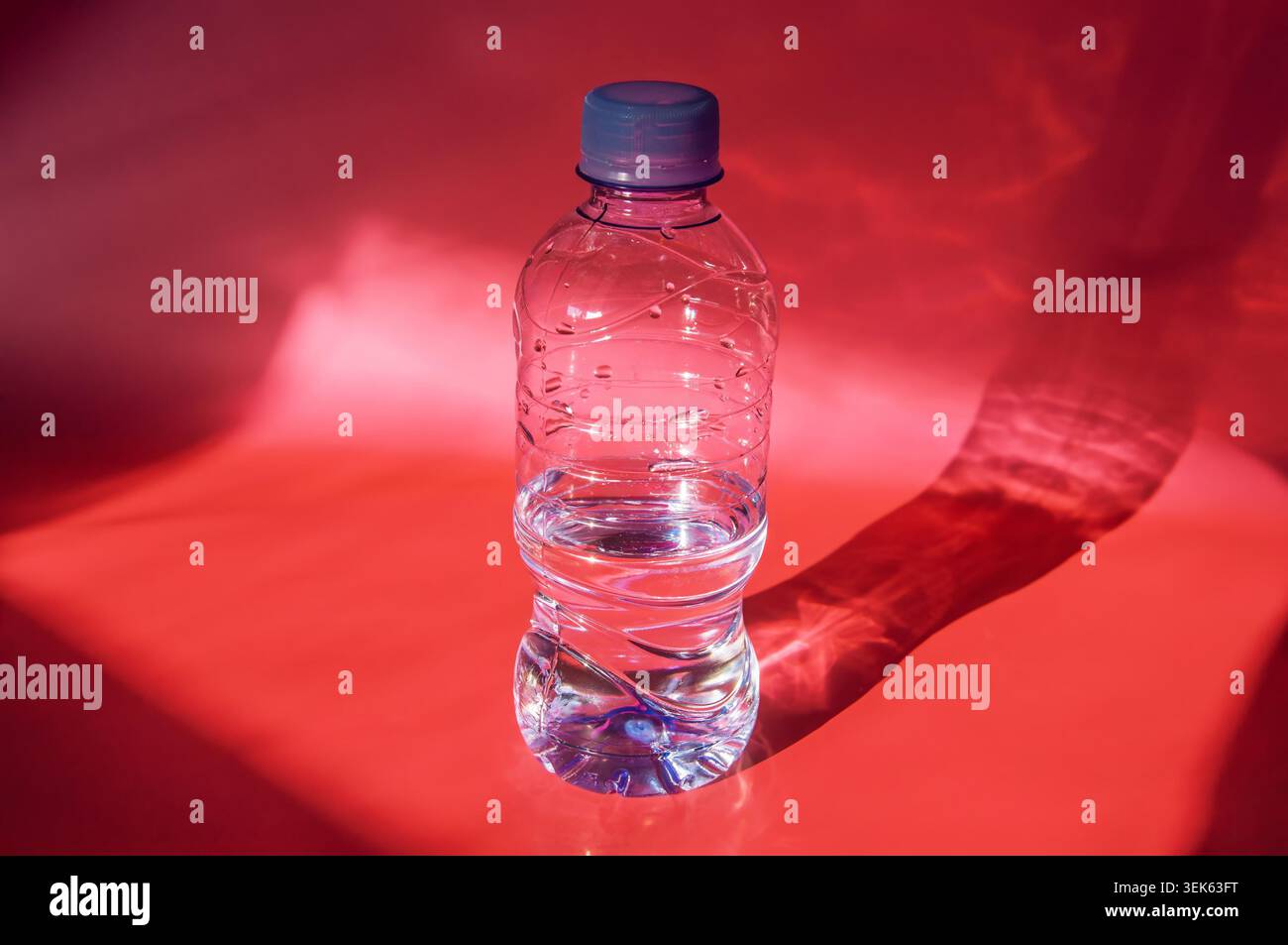 Clear plastic bottle filled with water casting a dramatic shadow on red background Stock Photo
