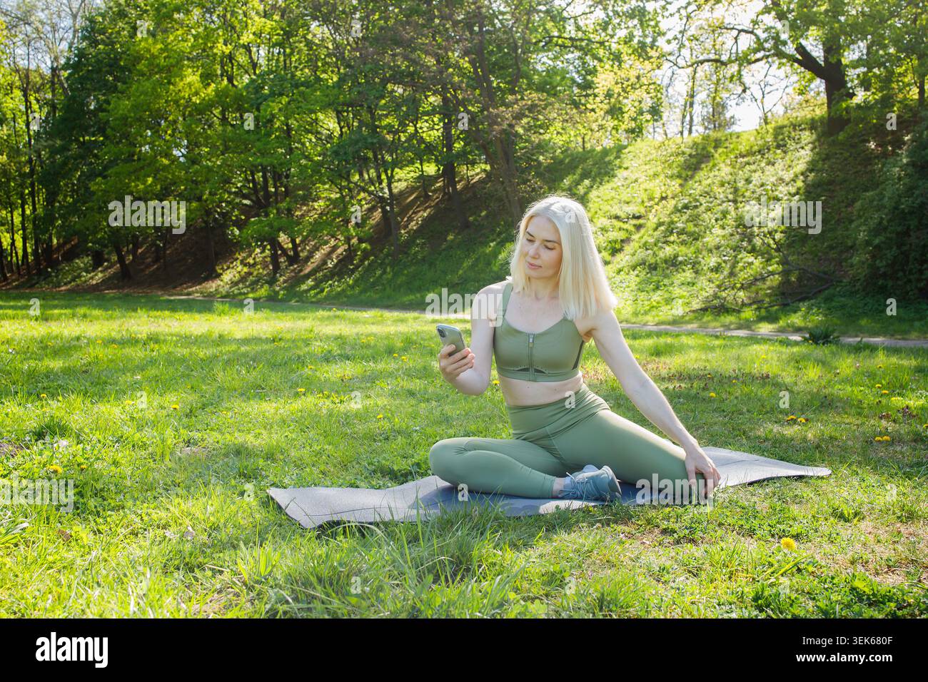 Blonde woman using smart phone during outdoor sport training in green Stock Photo