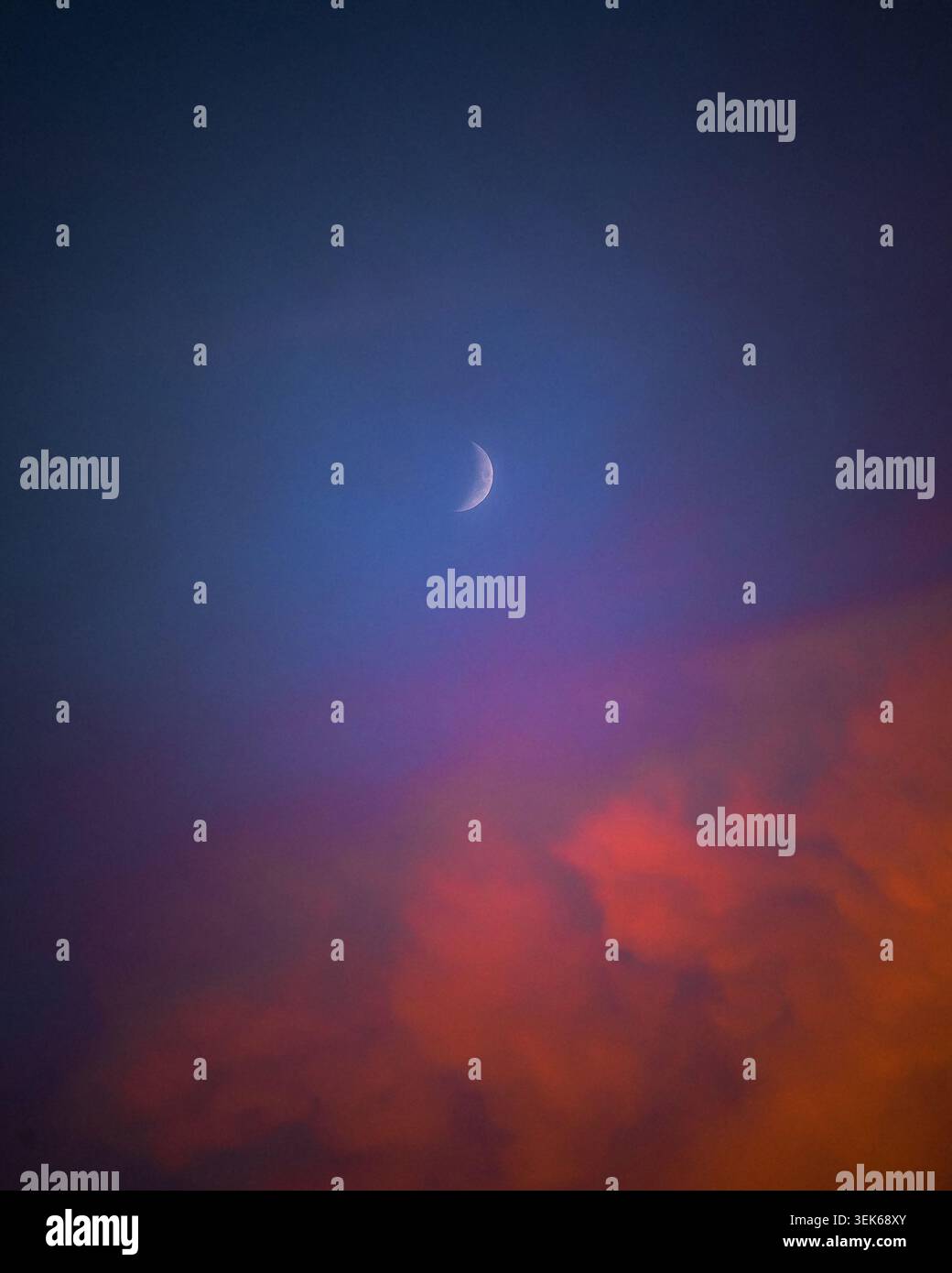 Waxing crescent moon above vibrant sunset clouds Stock Photo