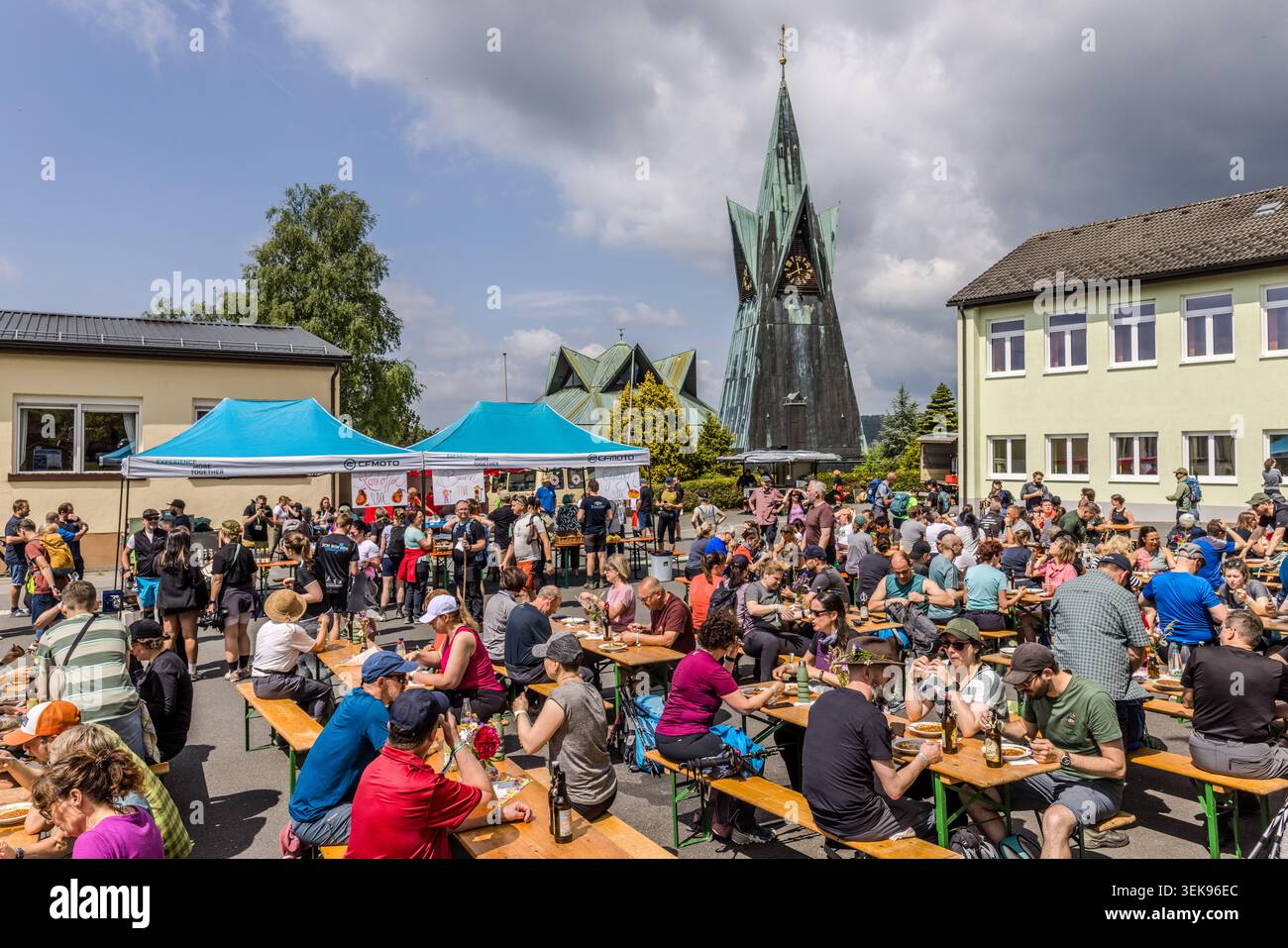 Lunch break in Buchbach: walkers are eating outdoors, with the tower of St Laurentius Church rising up in the background, Bavaria, Germany Stock Photo