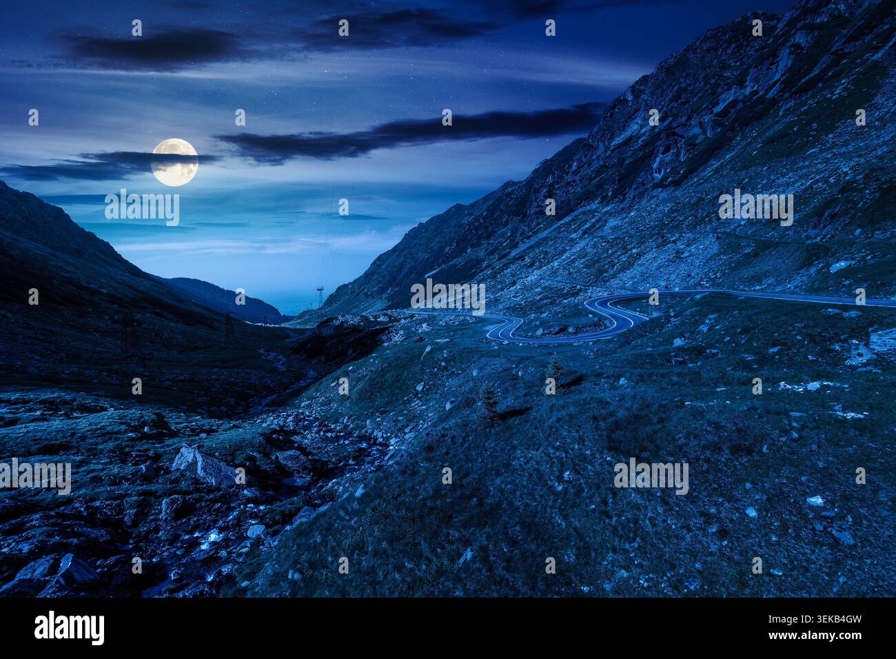 road through mountains winding uphill at night. full moon over popular highway travel destination of Romania. mysterious view of mountain on summertim Stock Photo