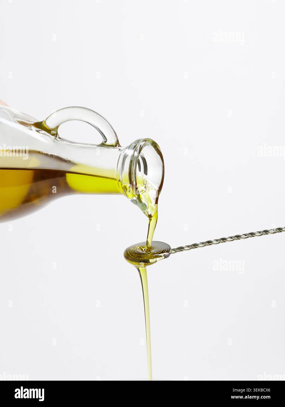 Olive oil dripping from glass bottle onto twisted cocktail spoon Stock Photo