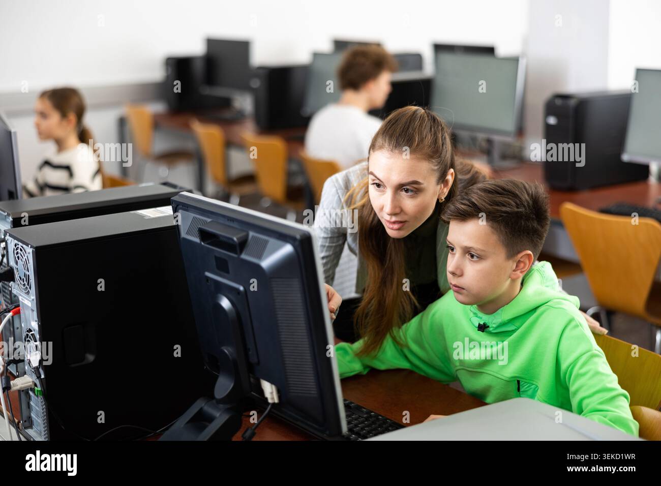 Female teacher consulting tween boy studying in computer class Stock Photo