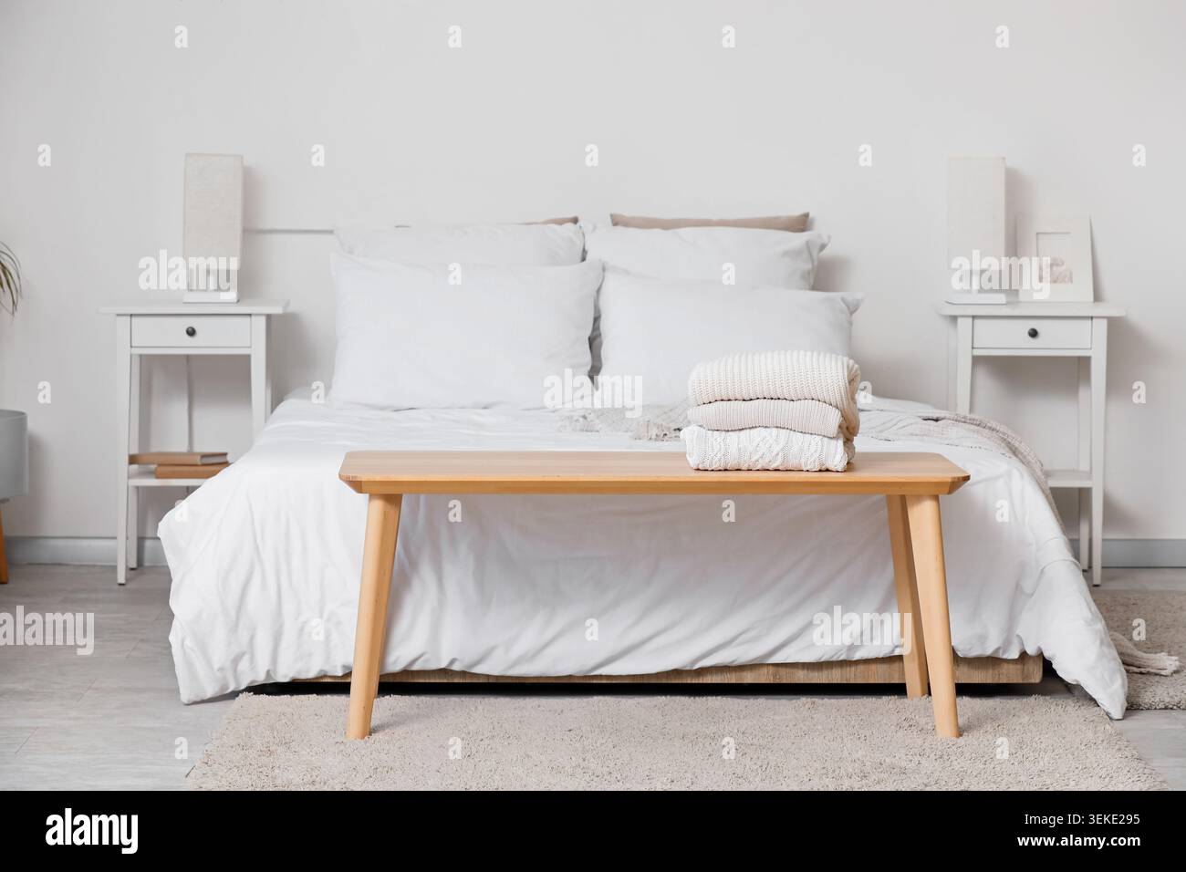 Stack of knitted sweaters on bedside bench in bedroom Stock Photo