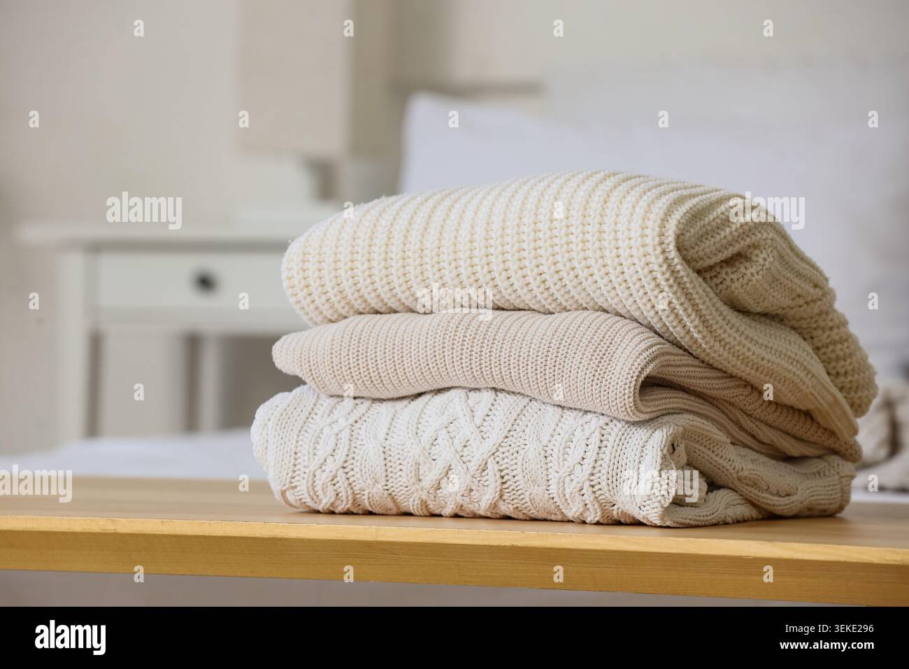 Stack of knitted sweaters on bedside bench in bedroom, closeup Stock Photo