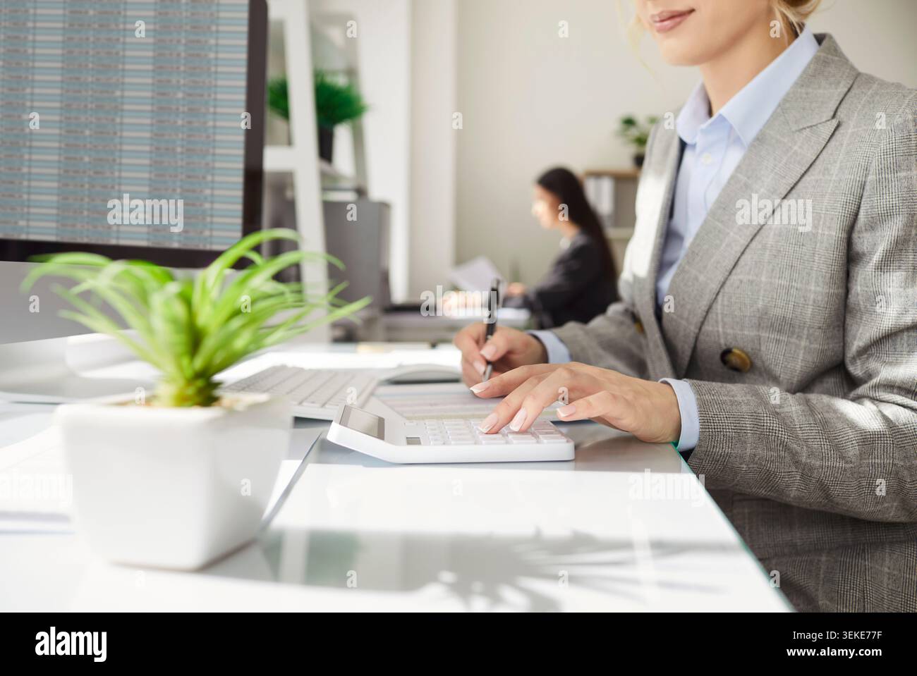 Businesswoman using calculator and taking notes while analyzing financial data on computer screen. Stock Photo