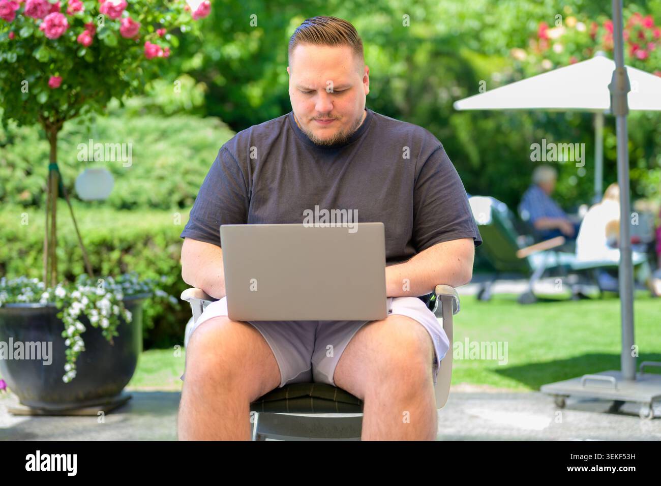 Young man working on a laptop outdoors in a sunny green garden. Authentic lifestyle and business image representing remote work, digital nomad lifesty Stock Photo