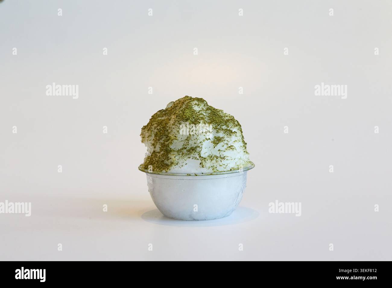 Matcha green tea shaved ice dessert in a clear plastic bowl on a white background. Stock Photo