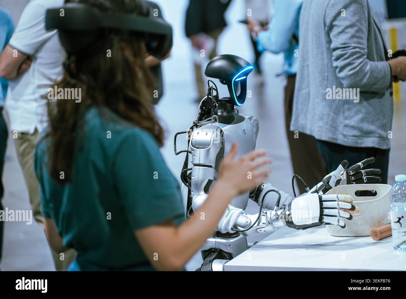 A young woman wearing a virtual reality headset controls a humanoid robot during a demonstration at an event. Stock Photo