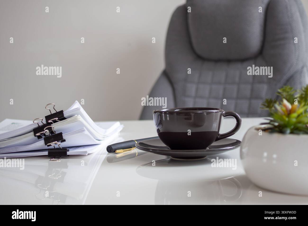 Dark ceramic cup sits on a sleek white desk Stock Photo