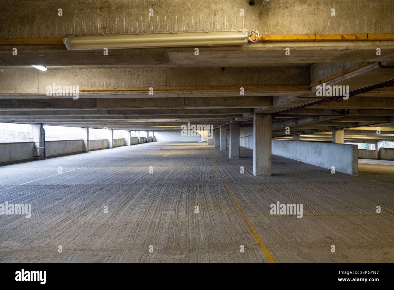 Empty concrete multi story car park with fluorescent lights, structural beams, and a striped floor Stock Photo