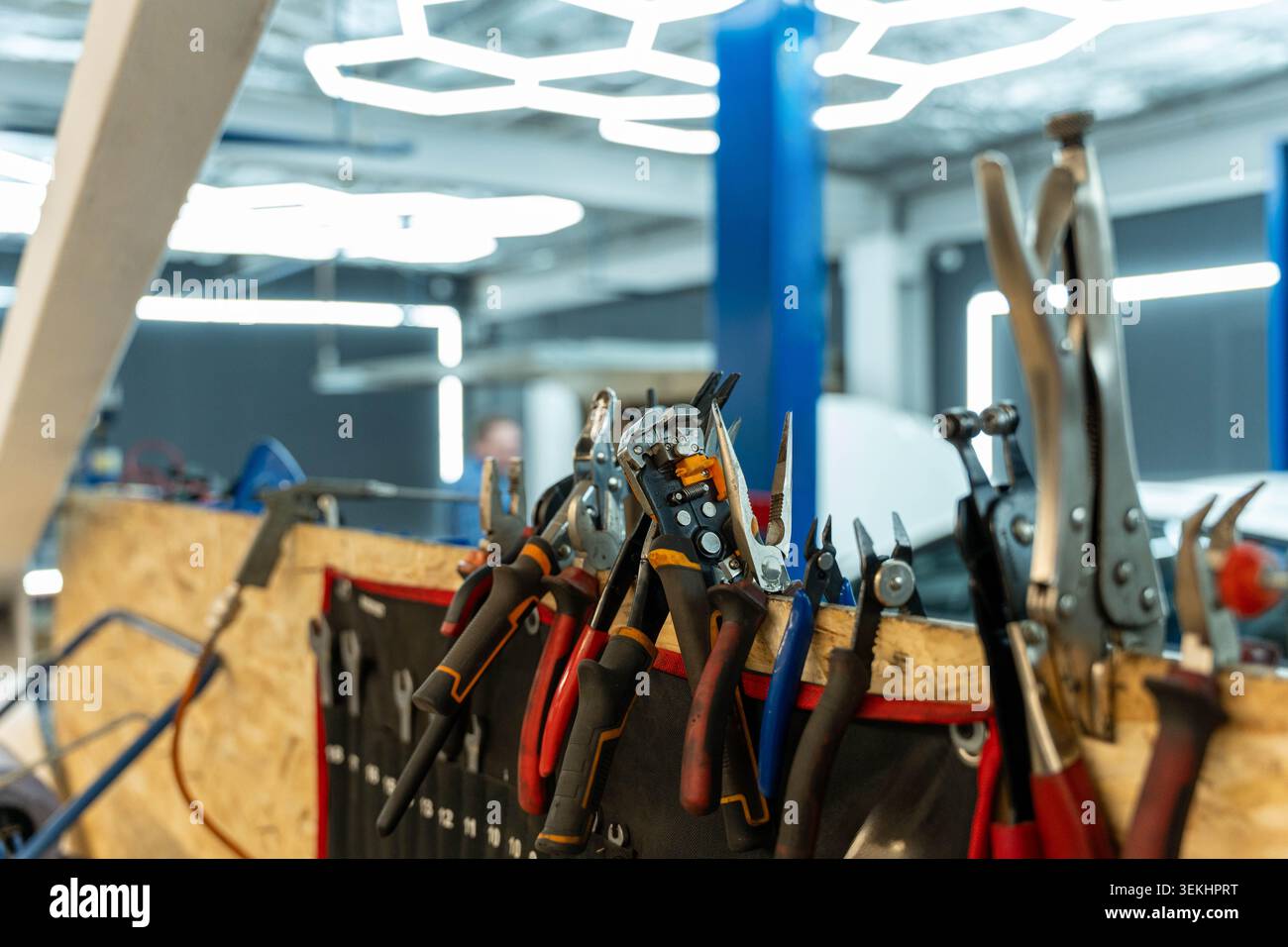 Assorted hand tools hang from and rest on a cluttered workbench in a bright modern workshop, with pliers, cutters, wrenches, and screwdrivers in the Stock Photo