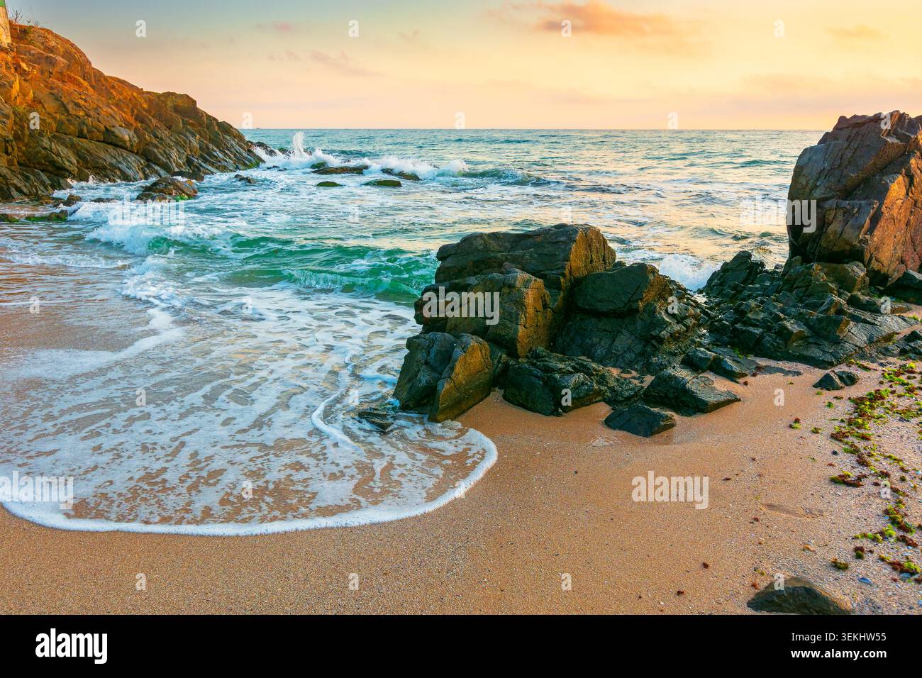 huge stones on the sandy beach at sunrise. wonderful holiday season background at the sea. clouds on the blue sky above horizon. view of waves washing Stock Photo