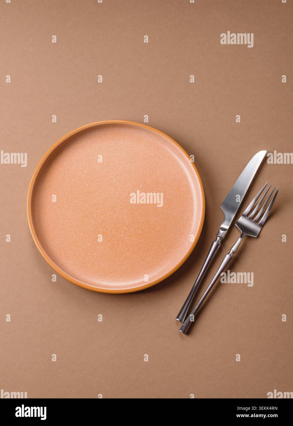 An empty round ceramic plate, knife, and fork as a dining table setting. An empty plate as a backdrop for your design Stock Photo