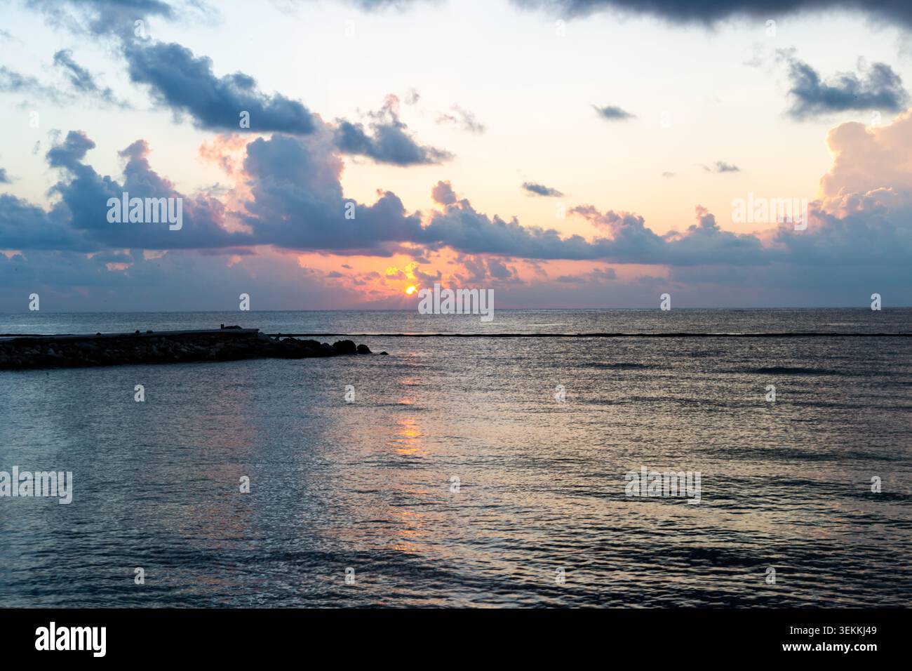 Sunrise over the ocean with dramatic storm clouds illuminated by golden sunlight, crepuscular rays spreading across the sky above calm tropical waters Stock Photo