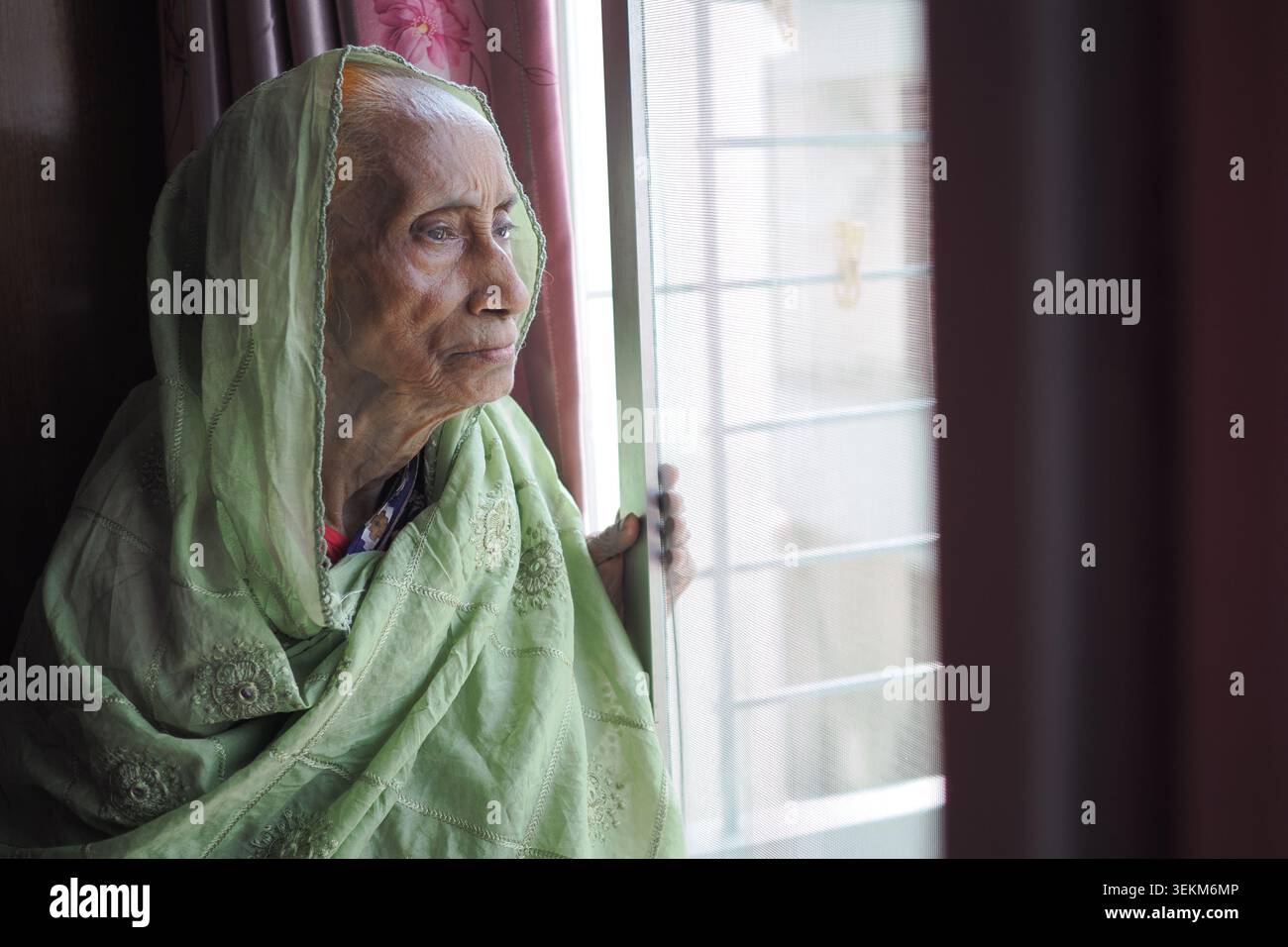 Elderly woman looking out of window in a home setting Stock Photo