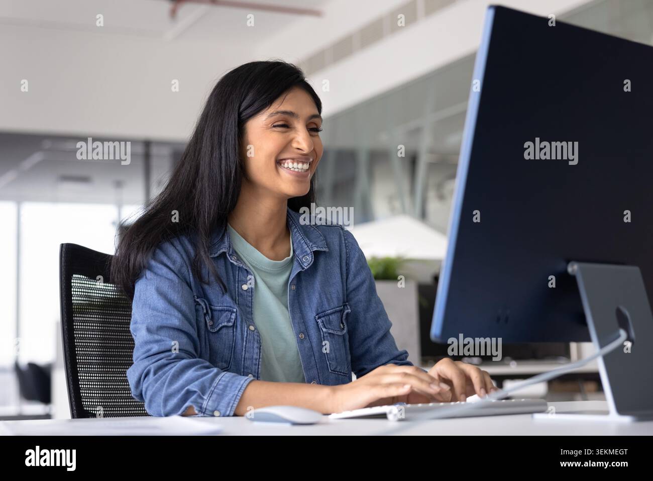 Happy Indian office employee working on computer in modern office Stock Photo