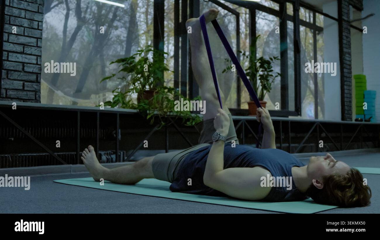 Young man lying on fitness mat performing resistance band leg exercise Stock Photo