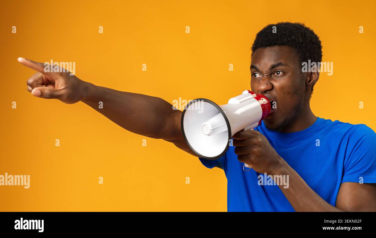 Person shouts through megaphone while pointing in a studio with orange background Stock Photo