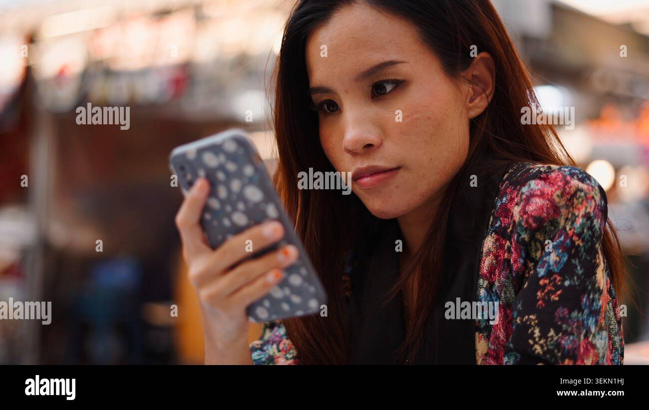 Young woman focusing on smartphone screen, browsing content outdoors Stock Photo