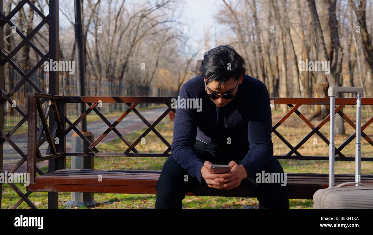 Pensive thoughtful young guy sitting on bench looking down sadly Stock Photo