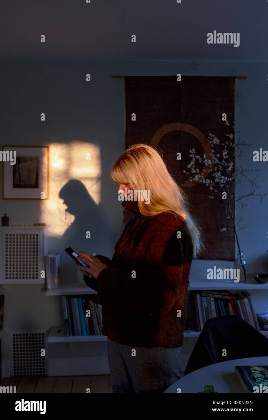 Blond woman using smart phone while standing at home Stock Photo
