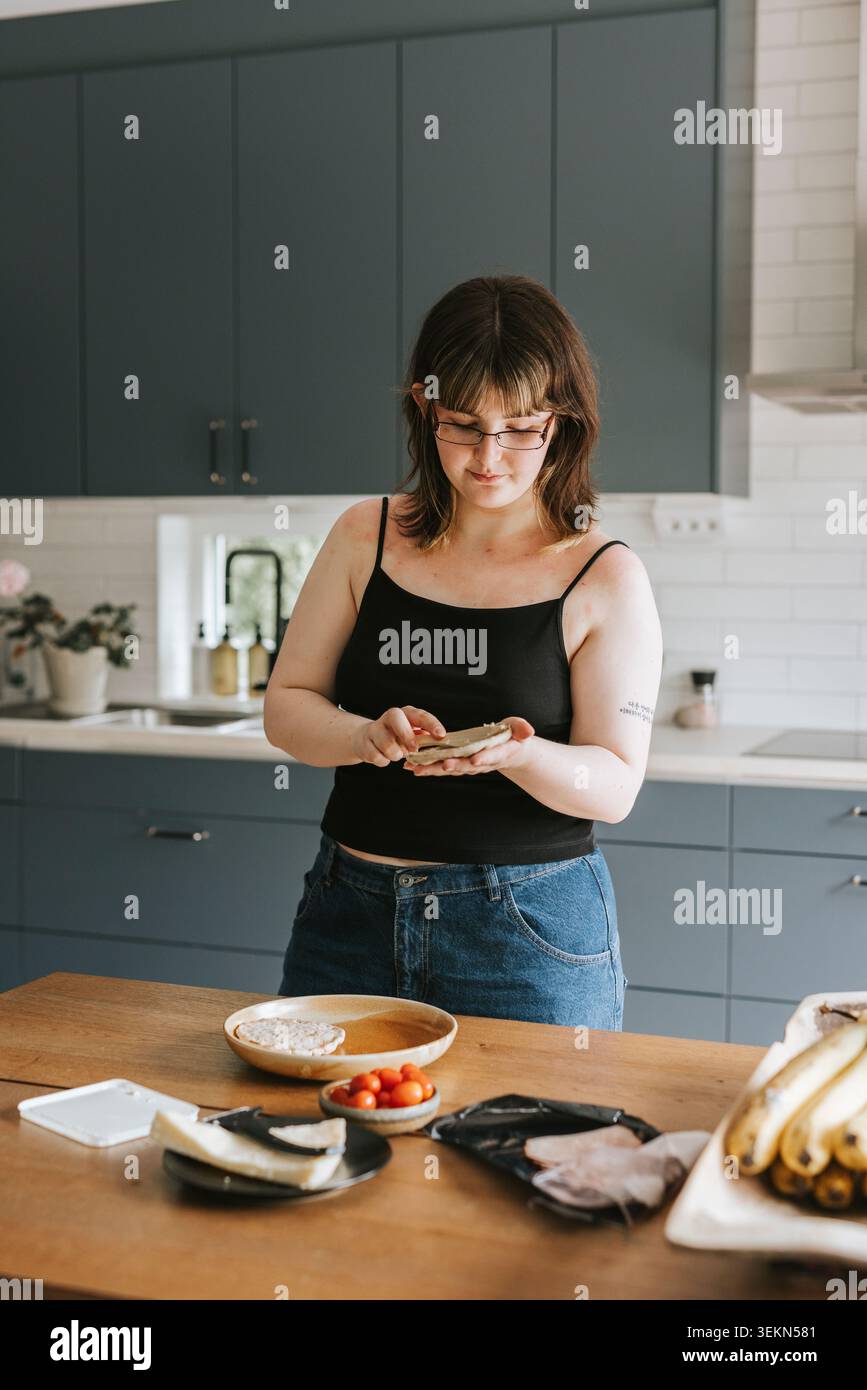 Young woman making breakfast while standing near table in kitchen at home Stock Photo