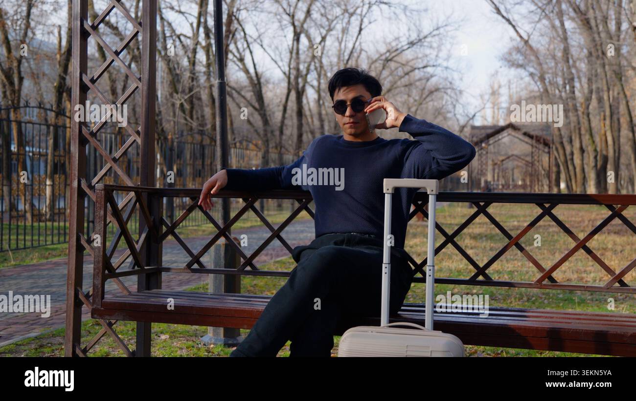 Relaxed confident handsome young man sitting on wooden bench Stock Photo