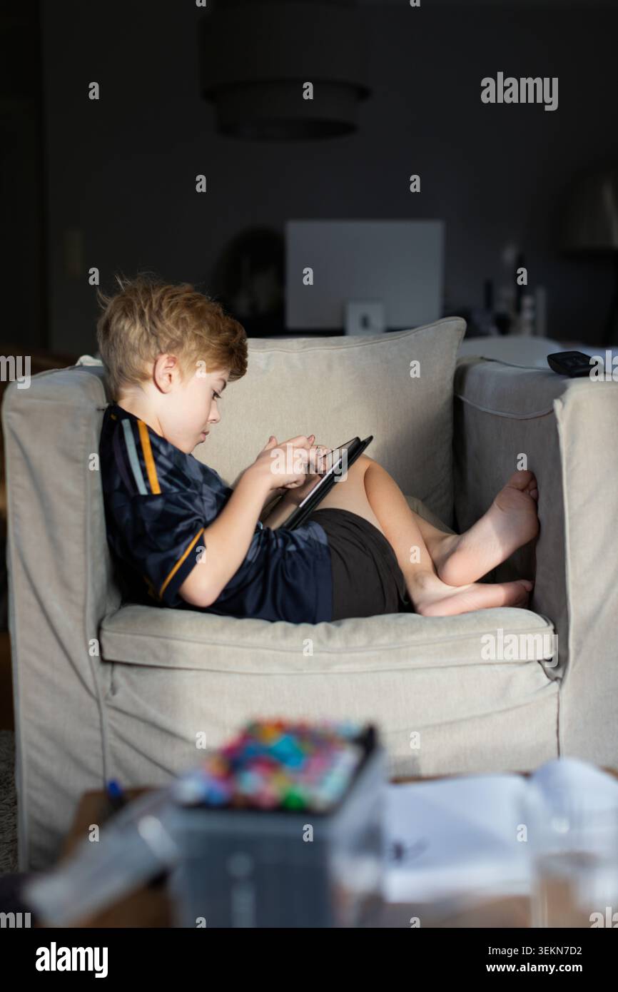 Side view of boy using digital tablet while sitting on sofa at home Stock Photo