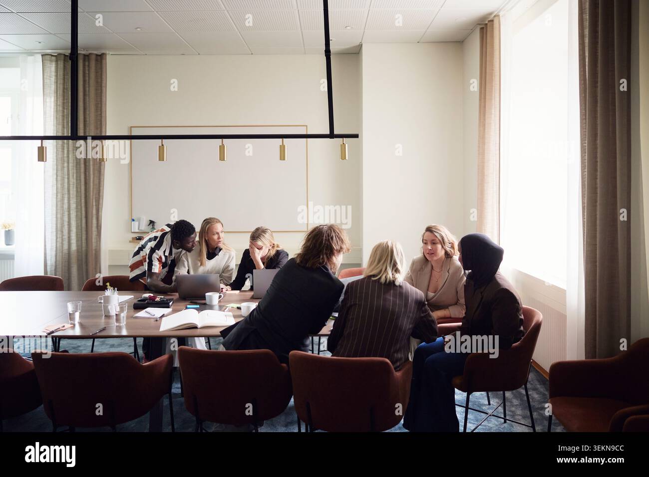 Male and female business professionals sharing marketing ideas while sitting in office meeting room Stock Photo