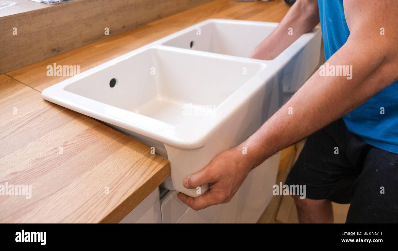 Precise And Efficient Sink Fixing Techniques Demonstrated. Demonstrating Skilled Craftsmanship In Setting Ceramic Sinks Into Surfaces Stock Photo