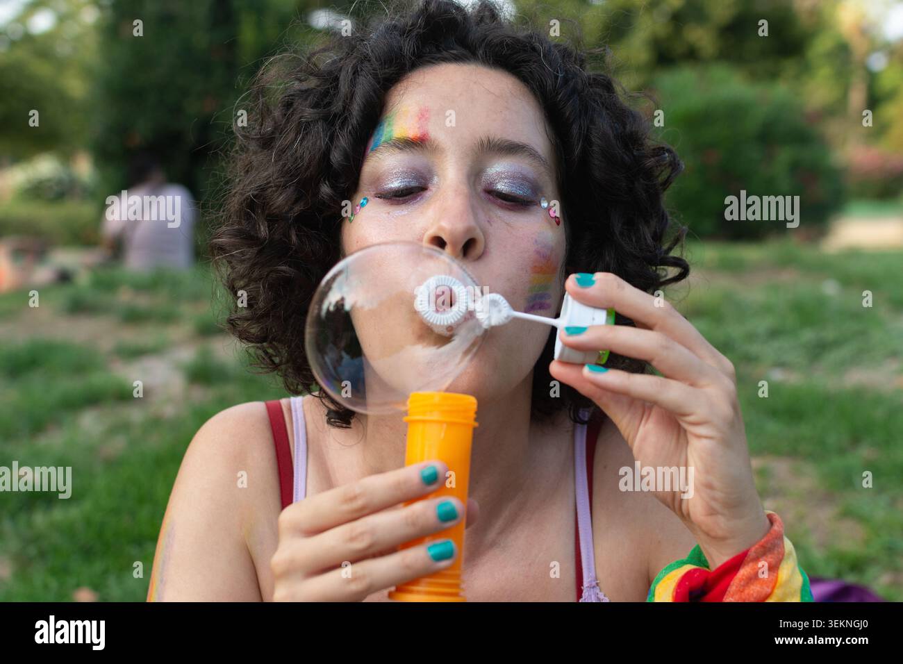 Queer person celebrating diversity blowing bubbles at park Stock Photo