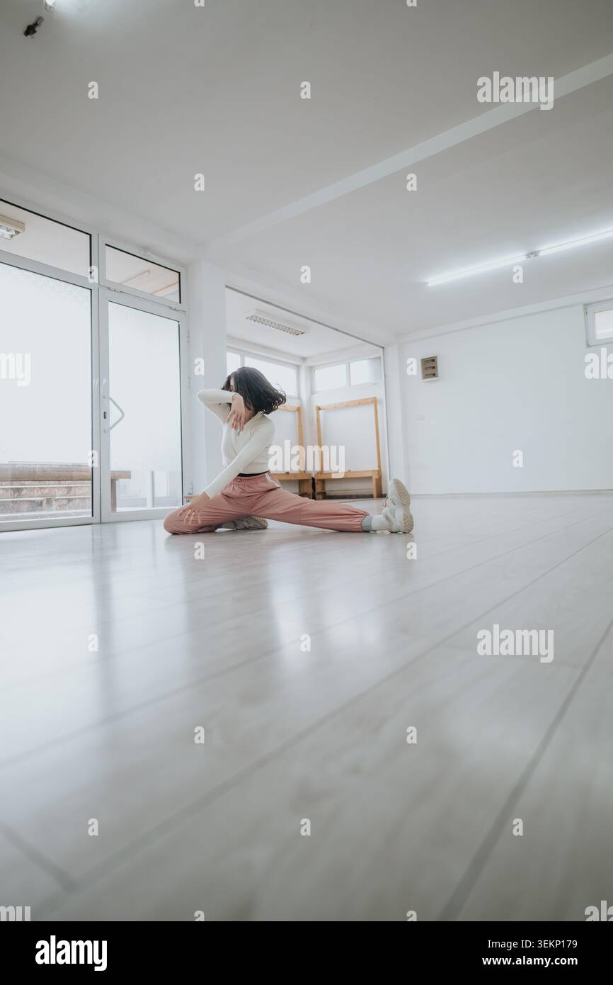 Dancer stretching in a bright empty studio practicing a graceful low split and contemporary pose Stock Photo